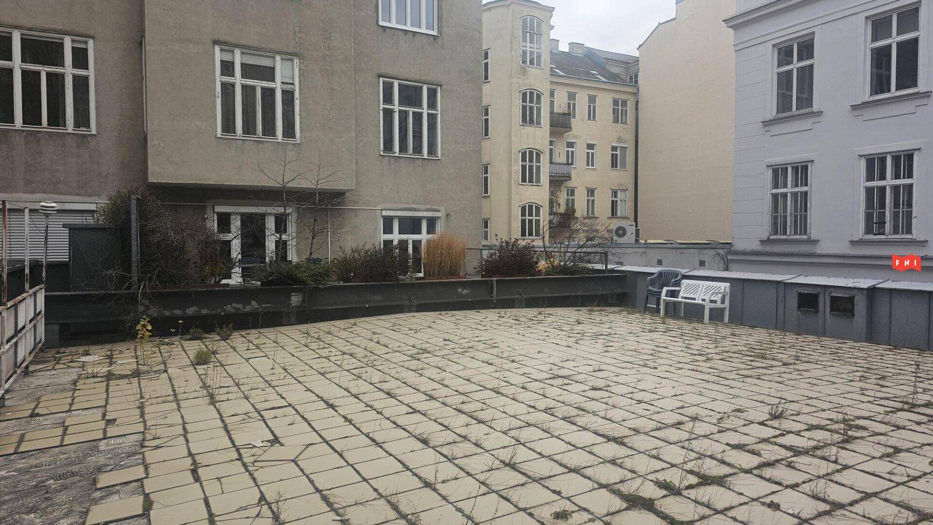 Große gepflasterte Terrasse im Hinterhof, umgeben von Gebäuden, mit Potenzial für Gestaltung.