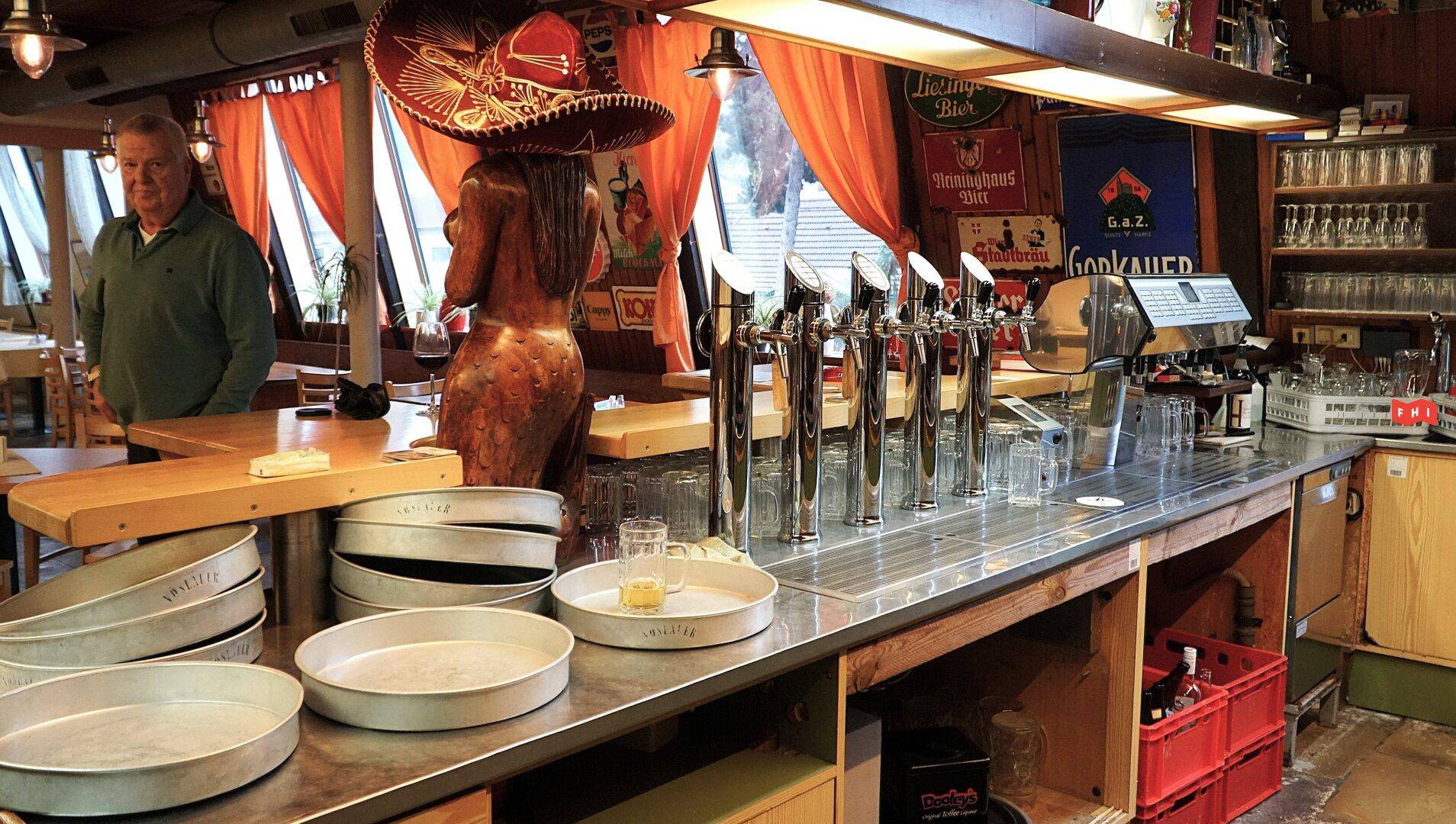 Lebhafte Bar mit Zapfanlage, Kaffeemaschine und einer dekorativen Statue, bereit für den Ausschank.
