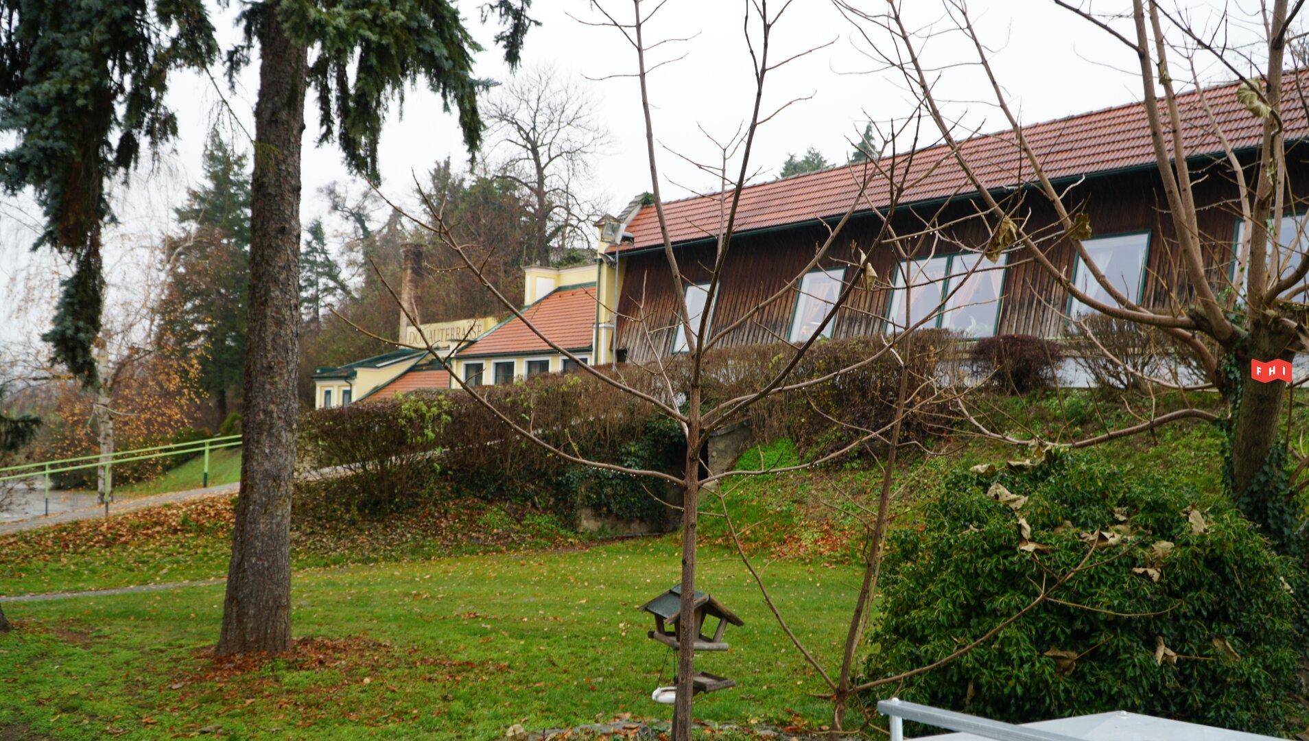 Gebäude mit Holzfassade und schrägen Fenstern, umgeben von einer grünen Wiese und Bäumen.