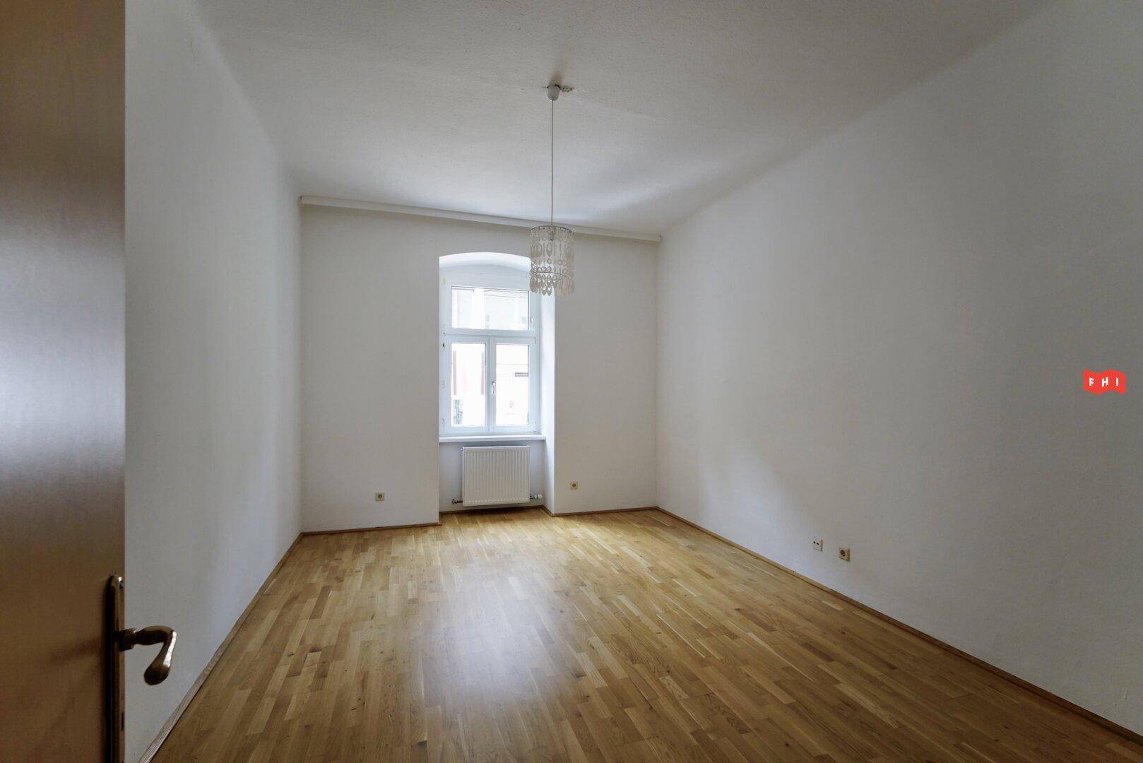 Helles, leeres Zimmer mit Parkettboden und einem Fenster, bereit zur individuellen Gestaltung.