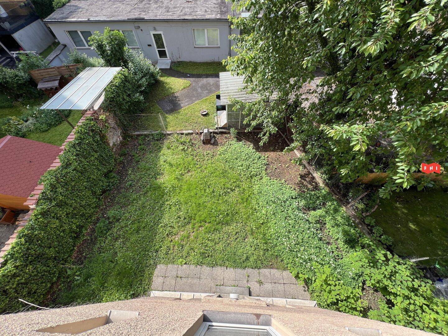 Blick von oben auf einen grünen Hinterhofgarten mit Rasenfläche und Bäumen.