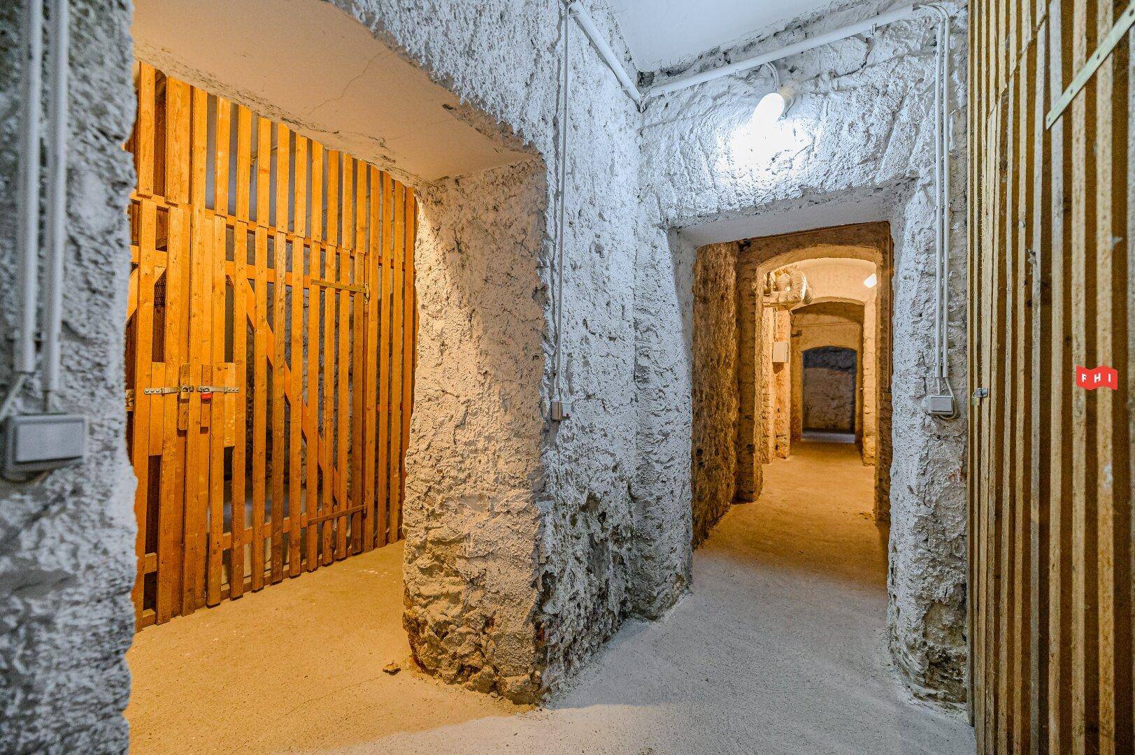 Rustikaler Kellergang mit Steinwänden und Holzverschlägen für Lagerzwecke.