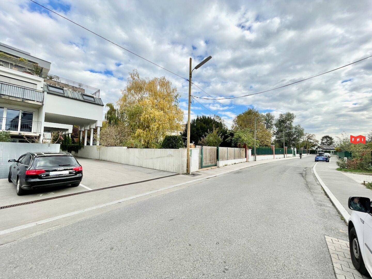 Straßenansicht eines modernen Wohnkomplexes mit geparkten Autos und Bäumen im herbstlichen Laub.