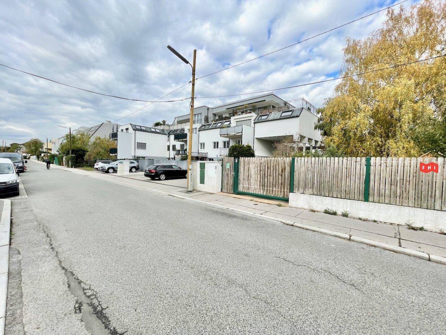 Weitläufige Straßenansicht eines modernen Wohnviertels mit mehreren Gebäuden und Herbstbäumen.