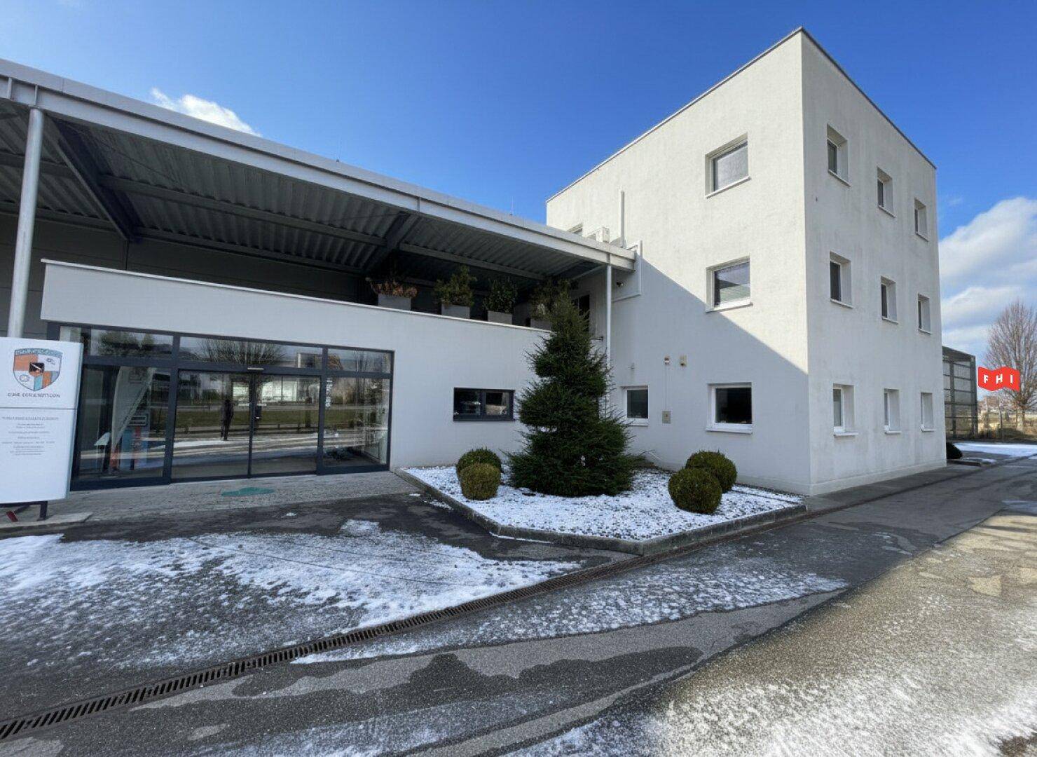Modernes weißes Gebäude mit großen Fenstern und gepflegter Außenanlage im Winter.