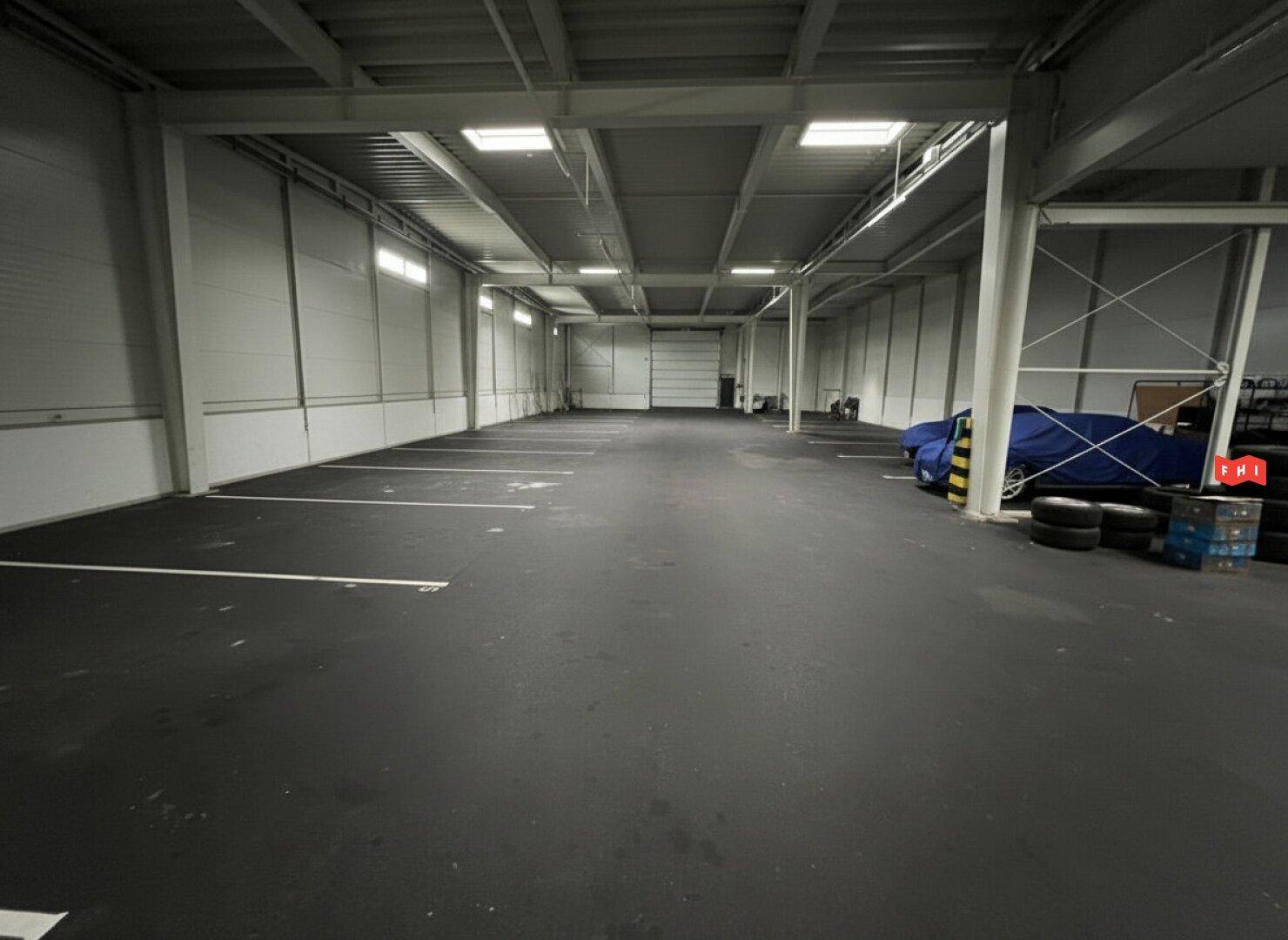 Geräumige Tiefgarage oder Lagerhalle mit markierten Parkplätzen und hoher Decke.