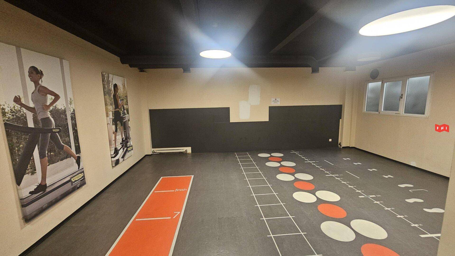 Funktionsbereich im Fitnessstudio mit markiertem Boden für Übungen und großen Wandpostern.