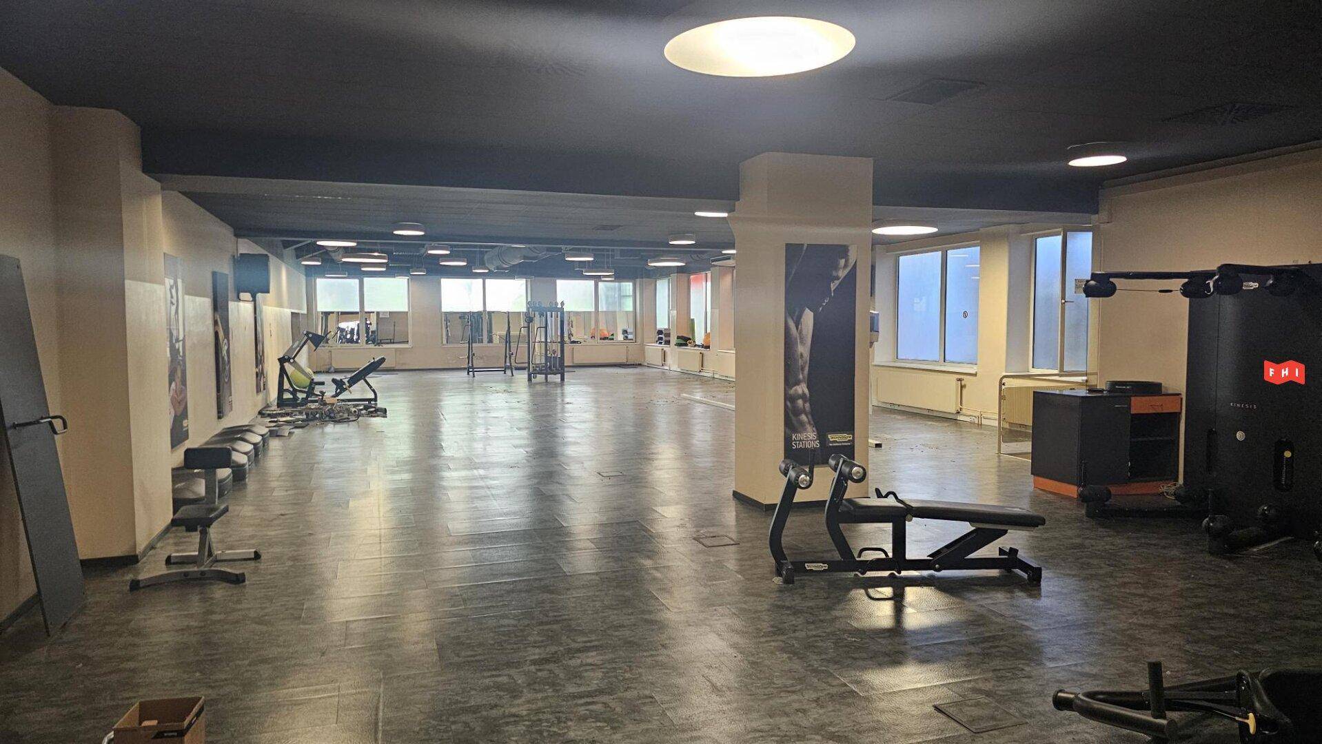 Geräumiger Fitnessraum mit verschiedenen Trainingsgeräten, großen Fenstern und dunklem Fliesenboden.