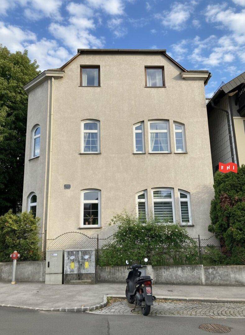 Vorderansicht eines Mehrfamilienhauses mit mehreren Fenstern und einem Roller vor dem Eingangsbereich.