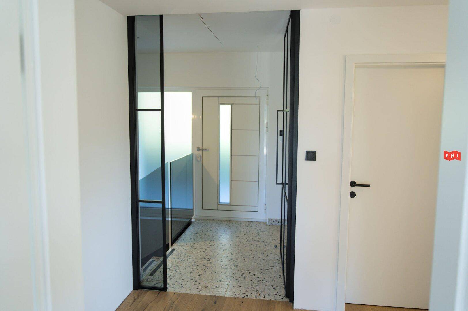 Moderner Eingangsbereich mit Glasabtrennung und Terrazzoboden, der zum Treppenhaus führt.
