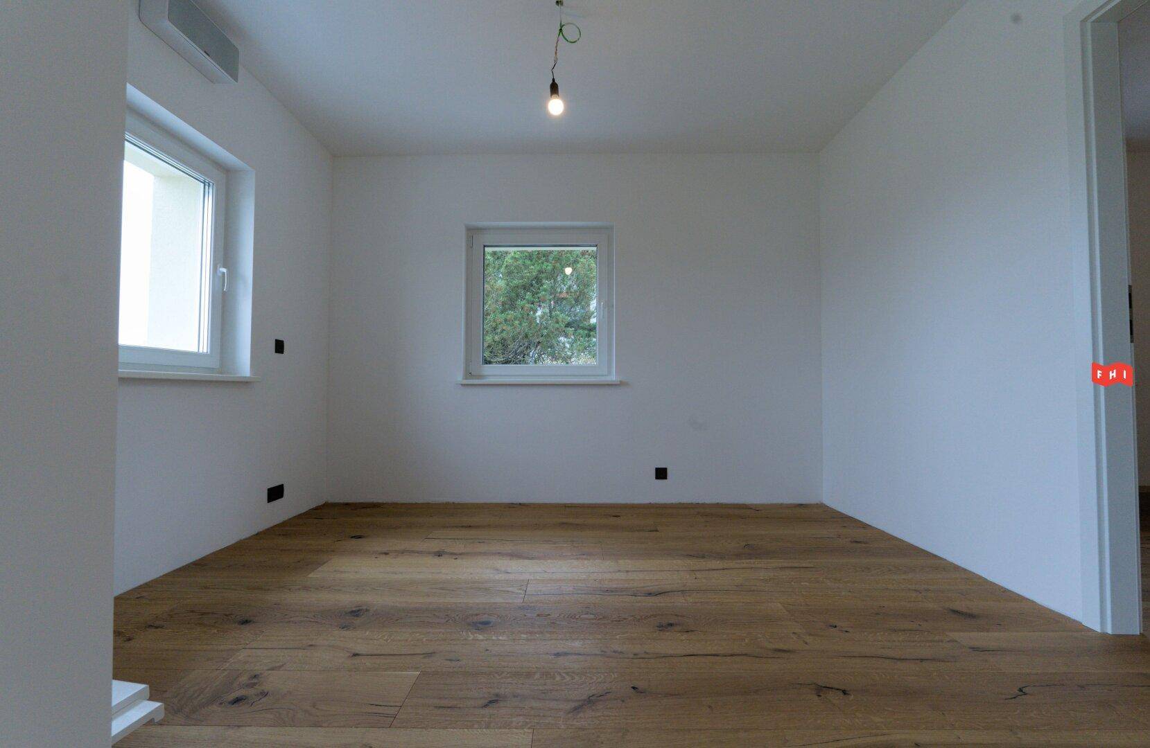 Ruhiges Schlafzimmer mit Holzboden und zwei Fenstern, die viel Tageslicht hereinlassen.