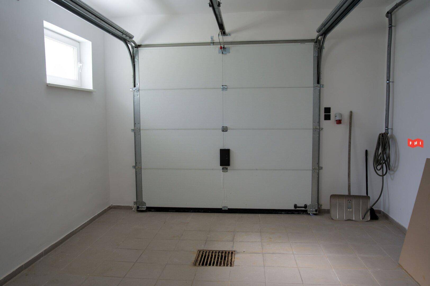 Geräumige Garage mit Sektionaltor, Fenster und Fliesenboden.