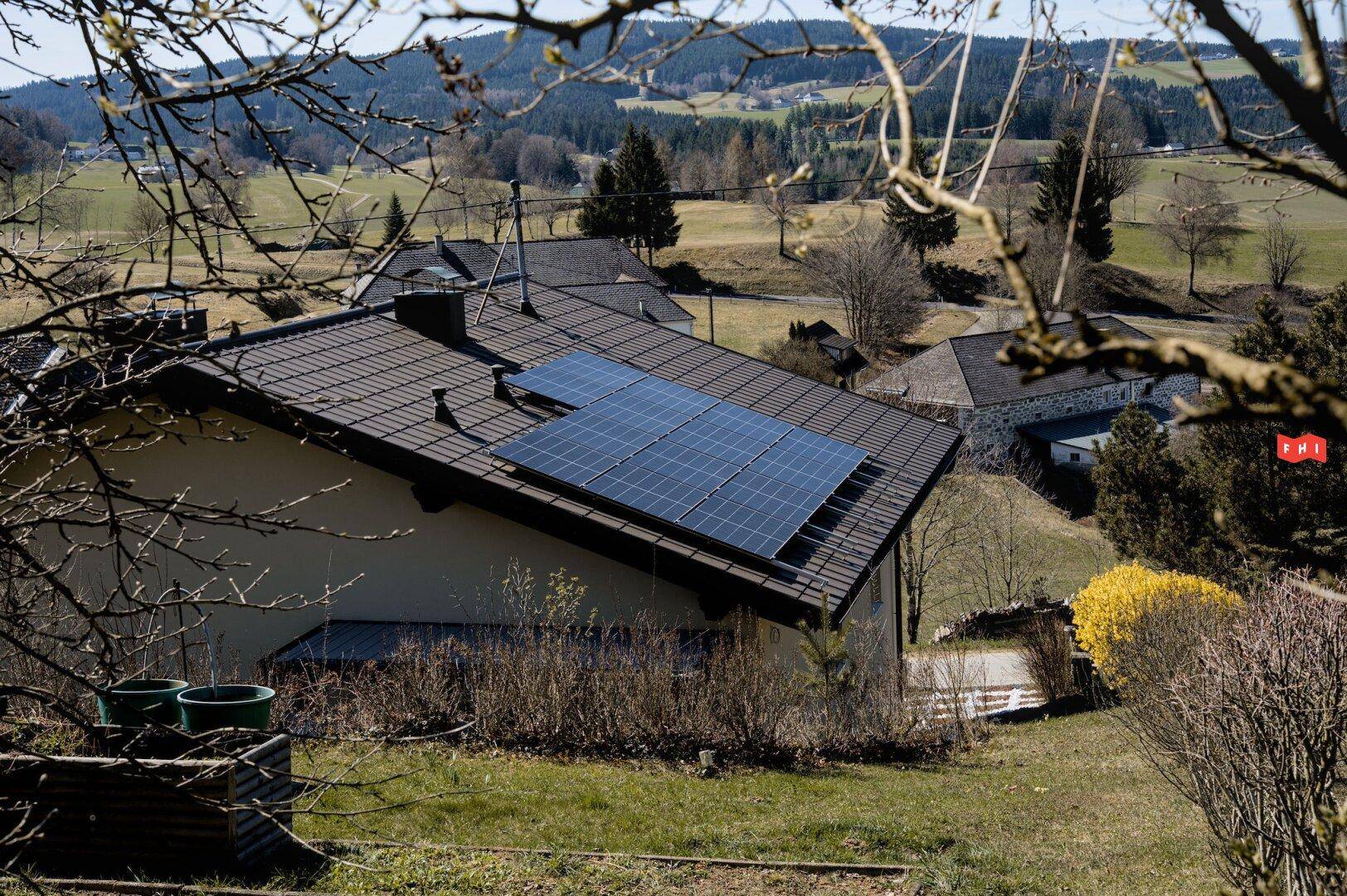 Dach des Hauses mit installierten Solarmodulen, umgeben von grüner Natur.