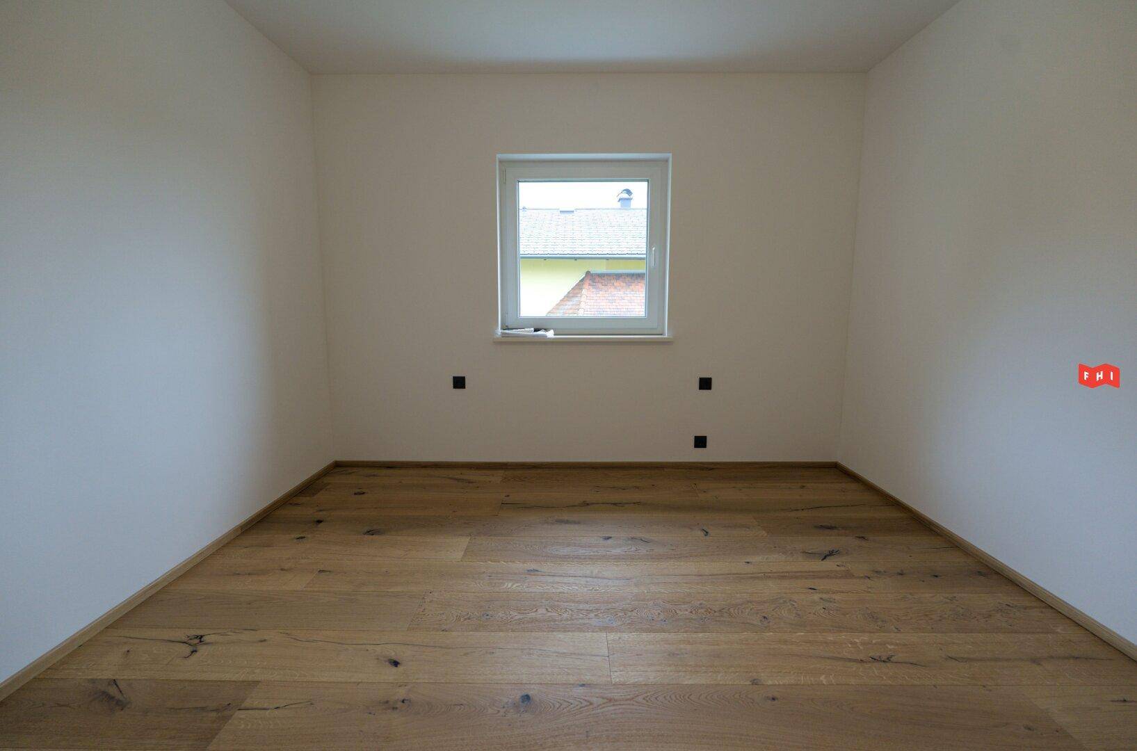 Helles, leeres Zimmer mit Holzboden und einem Fenster, ideal als Schlaf- oder Arbeitszimmer.