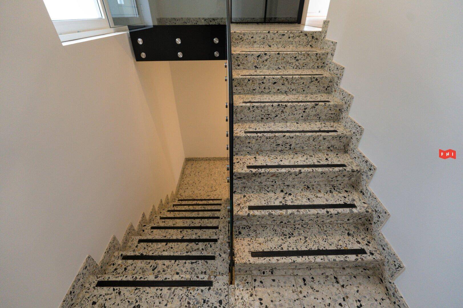 Treppenhaus mit gesprenkelten Steinstufen und modernem schwarzen Metallgeländer.