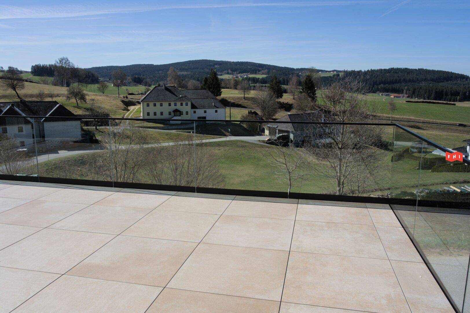 Detailansicht der modernen Terrasse mit hellen Fliesen und transparentem Glasgeländer.
