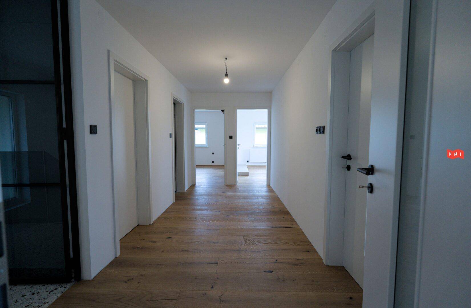 Langer, heller Flur mit elegantem Holzboden, der zu verschiedenen Zimmern führt.