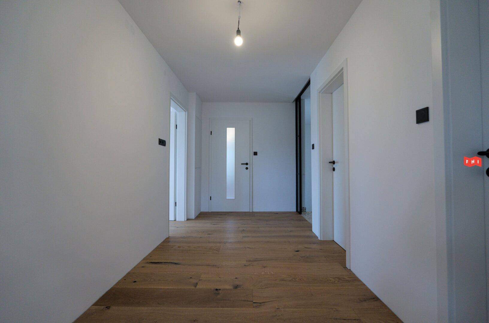 Heller Flur mit Holzboden und mehreren Türen, der zum Eingangsbereich führt.