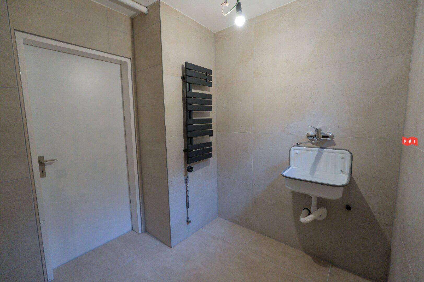 Funktionaler Raum mit kleinem Waschbecken und beheiztem Handtuchhalter an gefliesten Wänden.