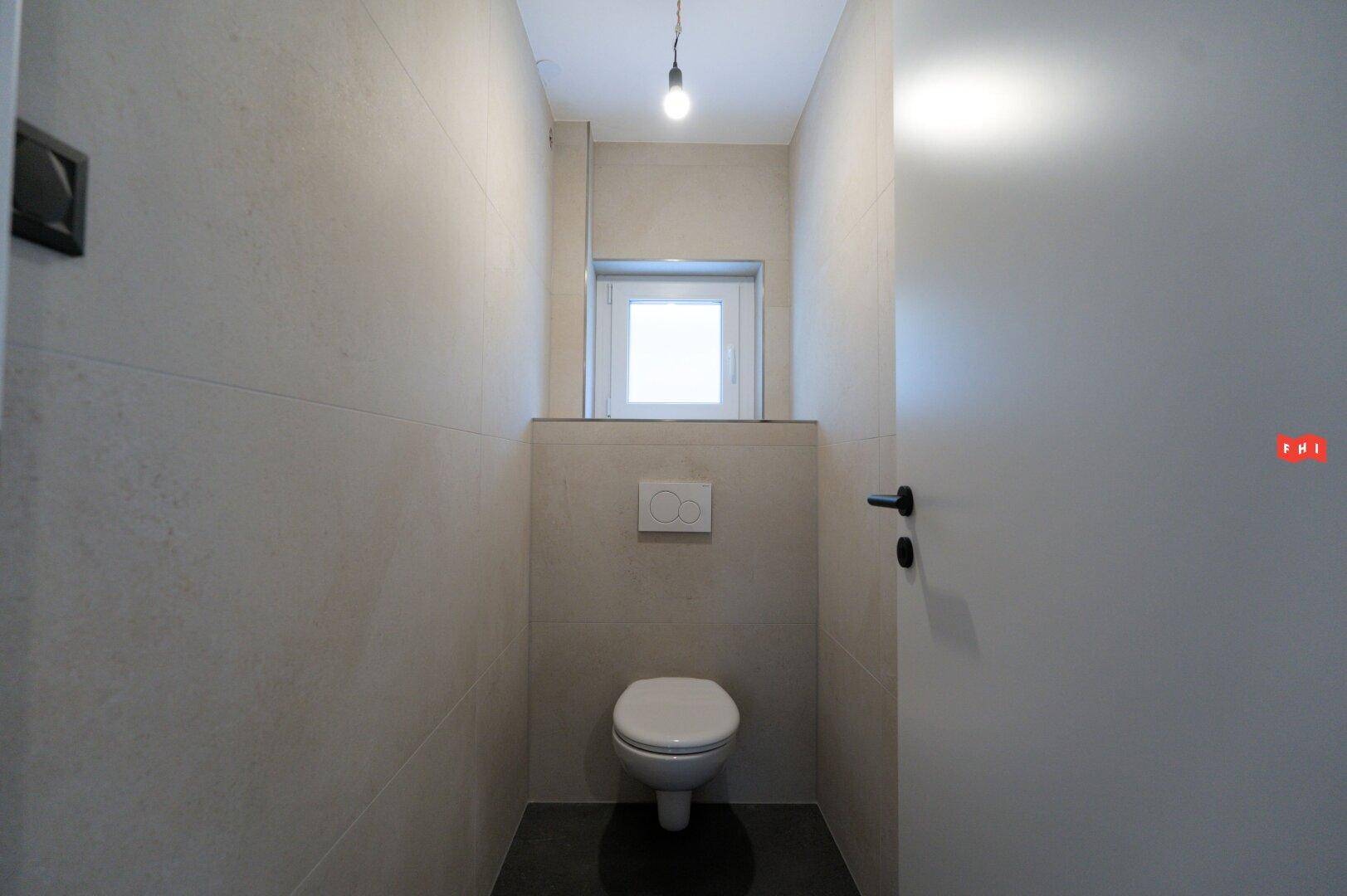 Modernes Gäste-WC mit wandhängender Toilette und kleinem Fenster für Tageslicht.