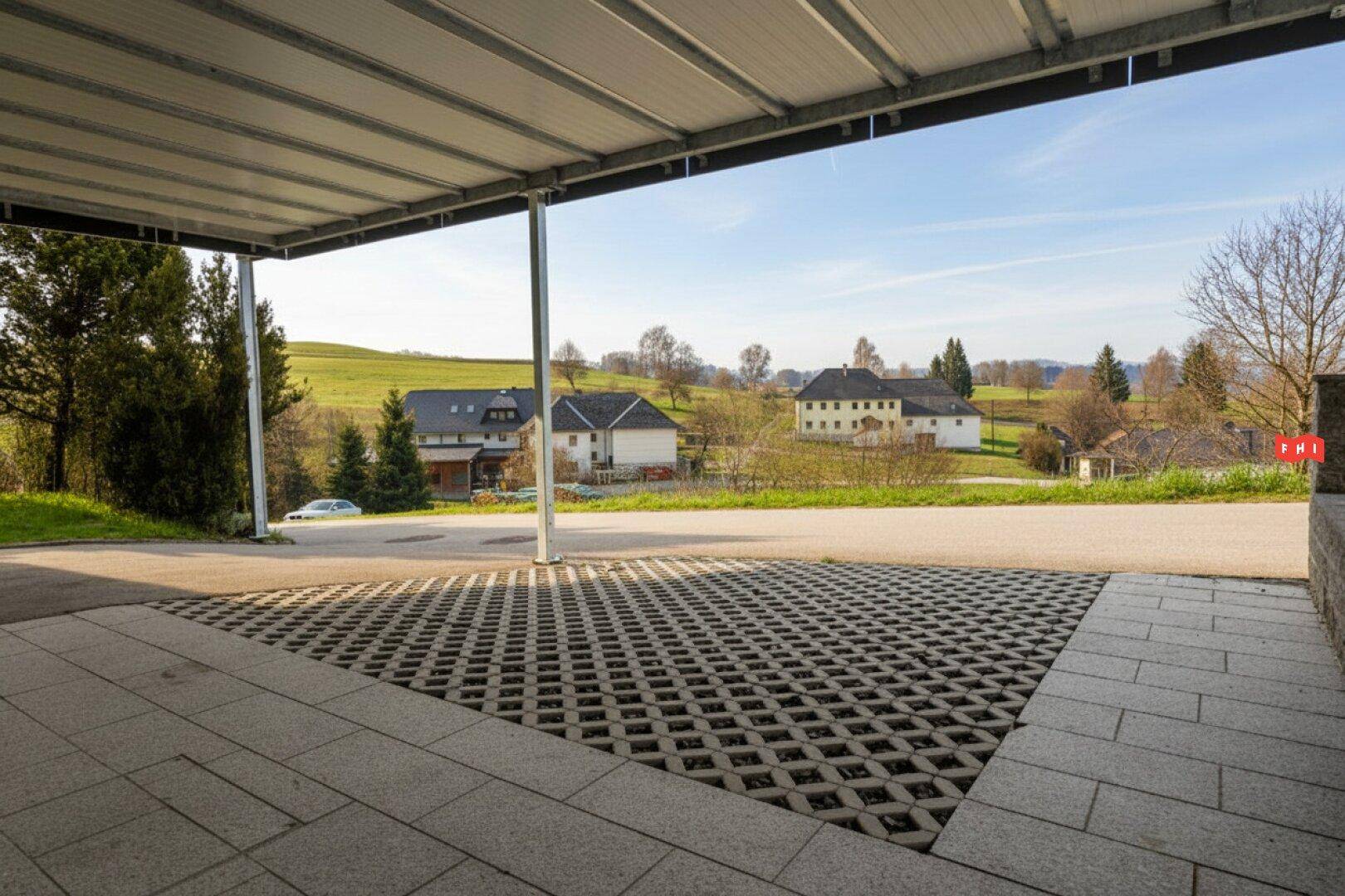 Überdachter Parkplatz mit Blick auf die umliegende grüne Landschaft und weitere Häuser.