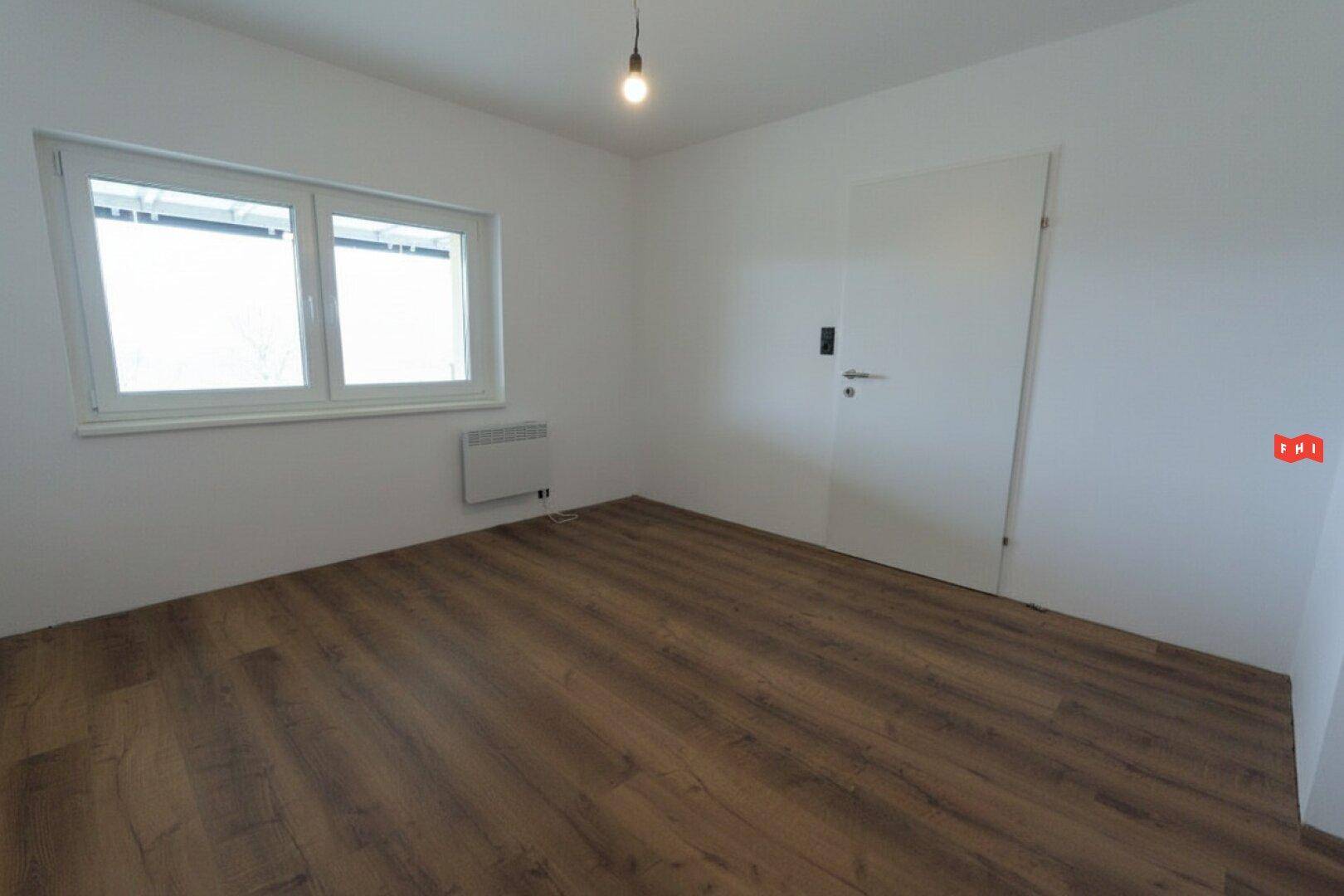 Leerer Raum mit Laminatboden, weißen Wänden und einem Fenster, bereit zur Einrichtung.