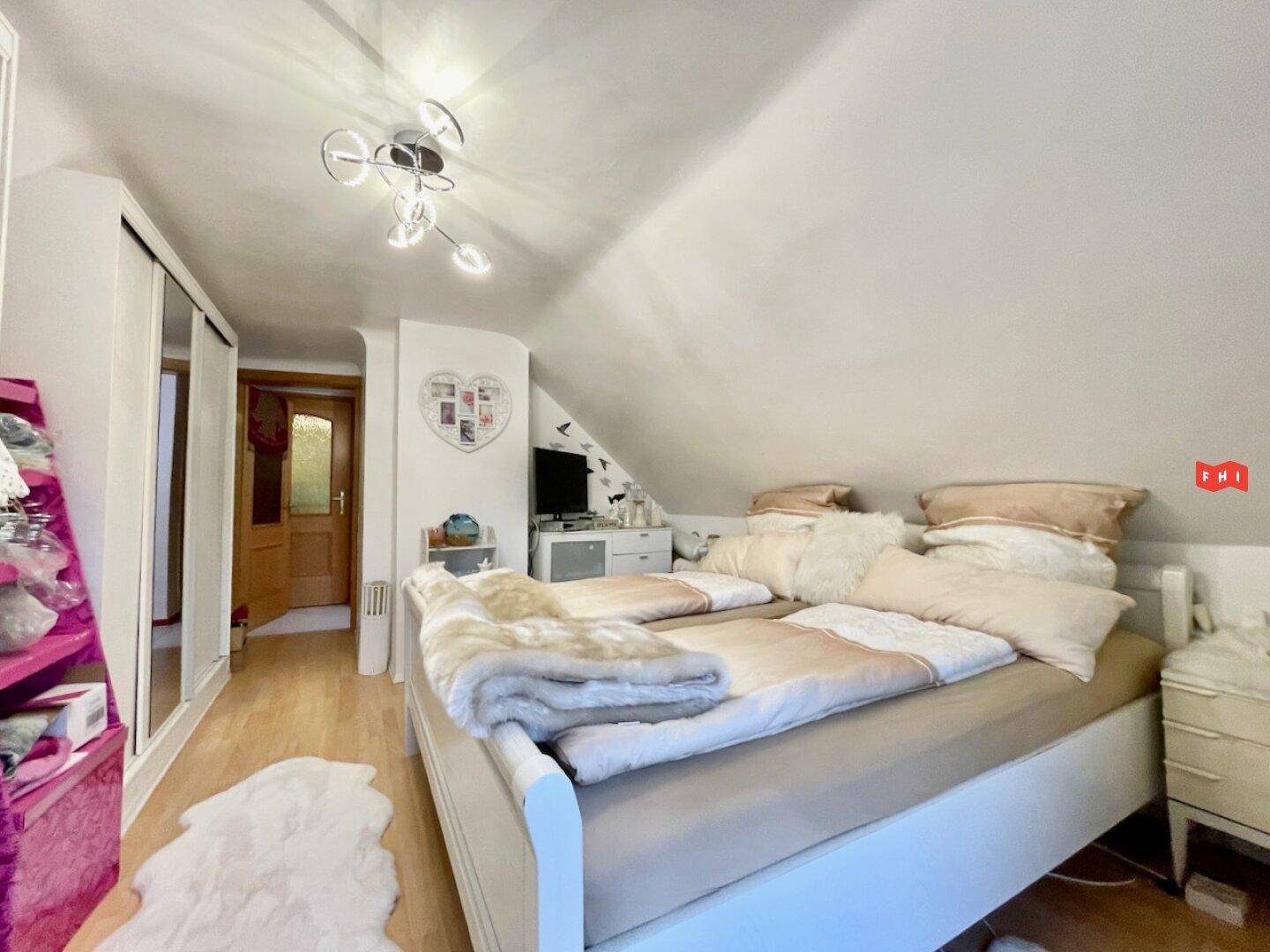 Helles Schlafzimmer im Dachgeschoss mit Laminatboden, Kleiderschrank und schrägen Wänden.