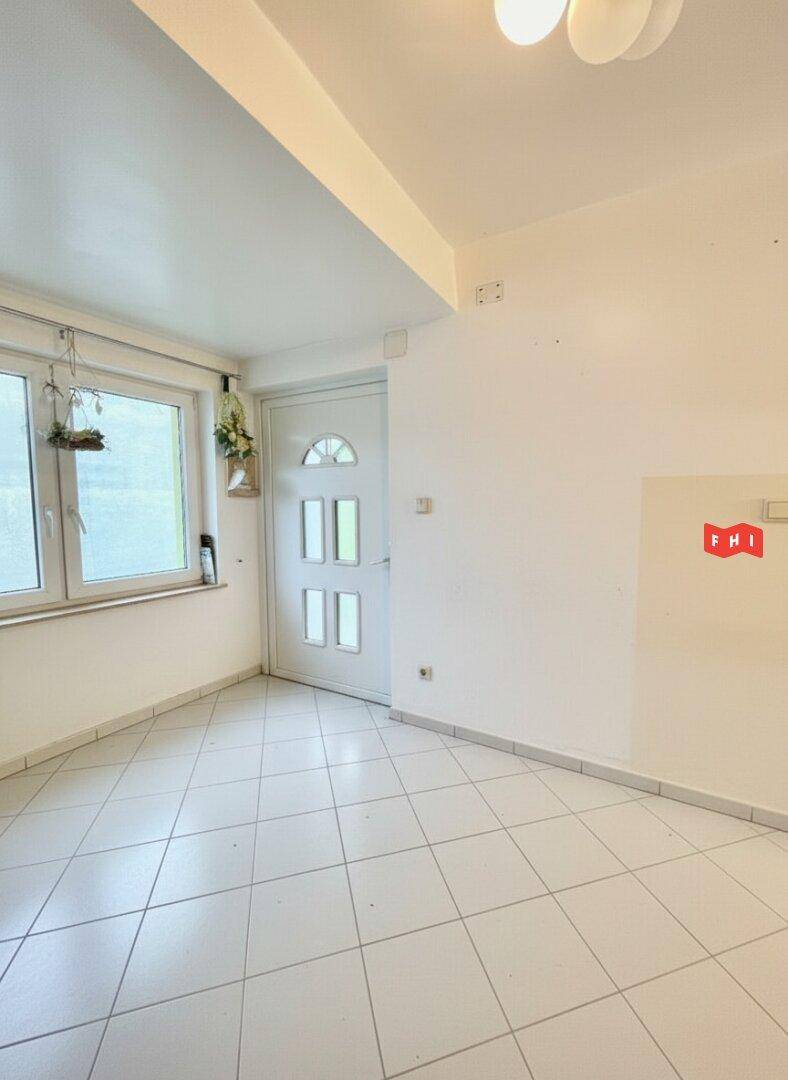 Heller Eingangsbereich mit weißen Fliesen, Fenster und einer weißen Haustür.