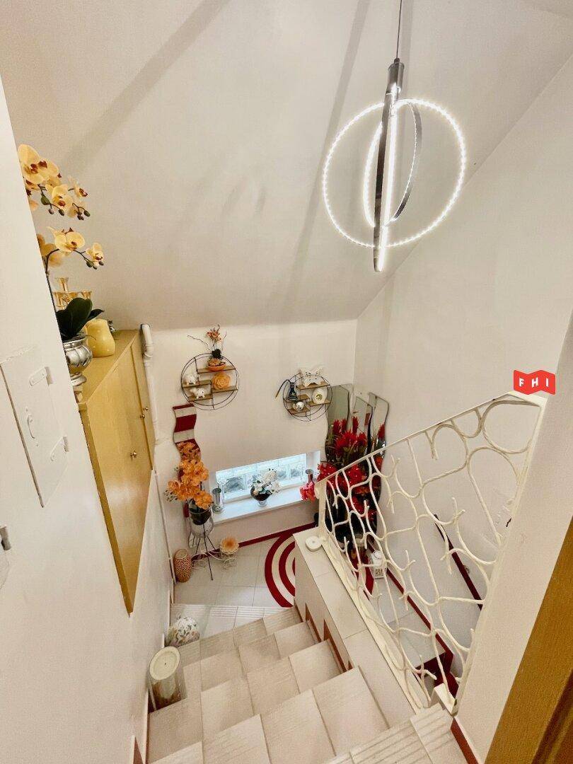 Treppenhaus mit modernem Kronleuchter, weißem Geländer und Dekoration an den Wänden.