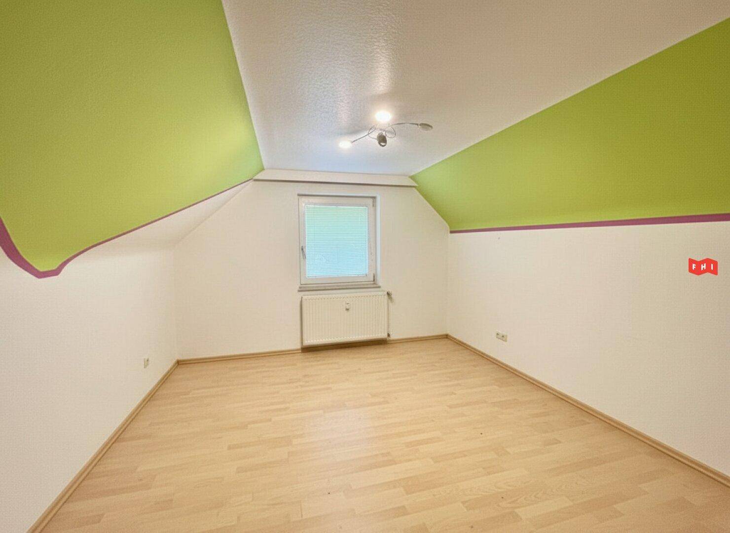 Leeres Zimmer im Dachgeschoss mit Laminatboden, Fenster und farbigen Wänden.