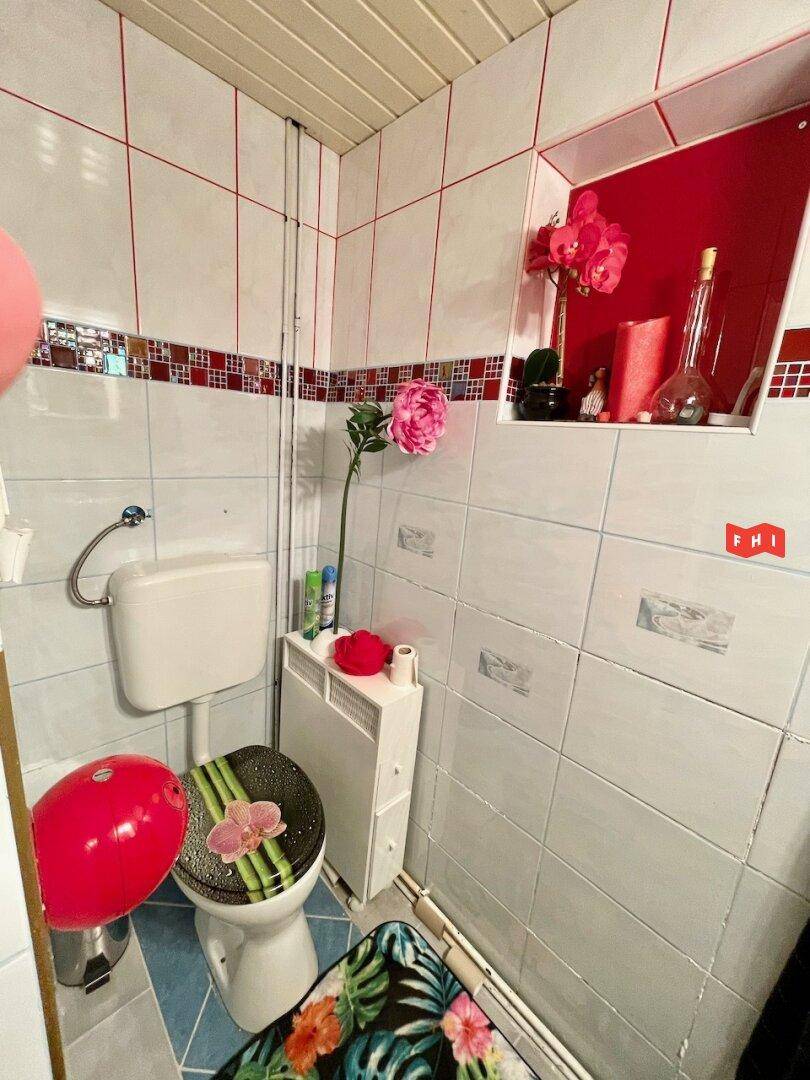 Kleines WC mit weißen Fliesen, farbigen Akzenten und floraler Dekoration.