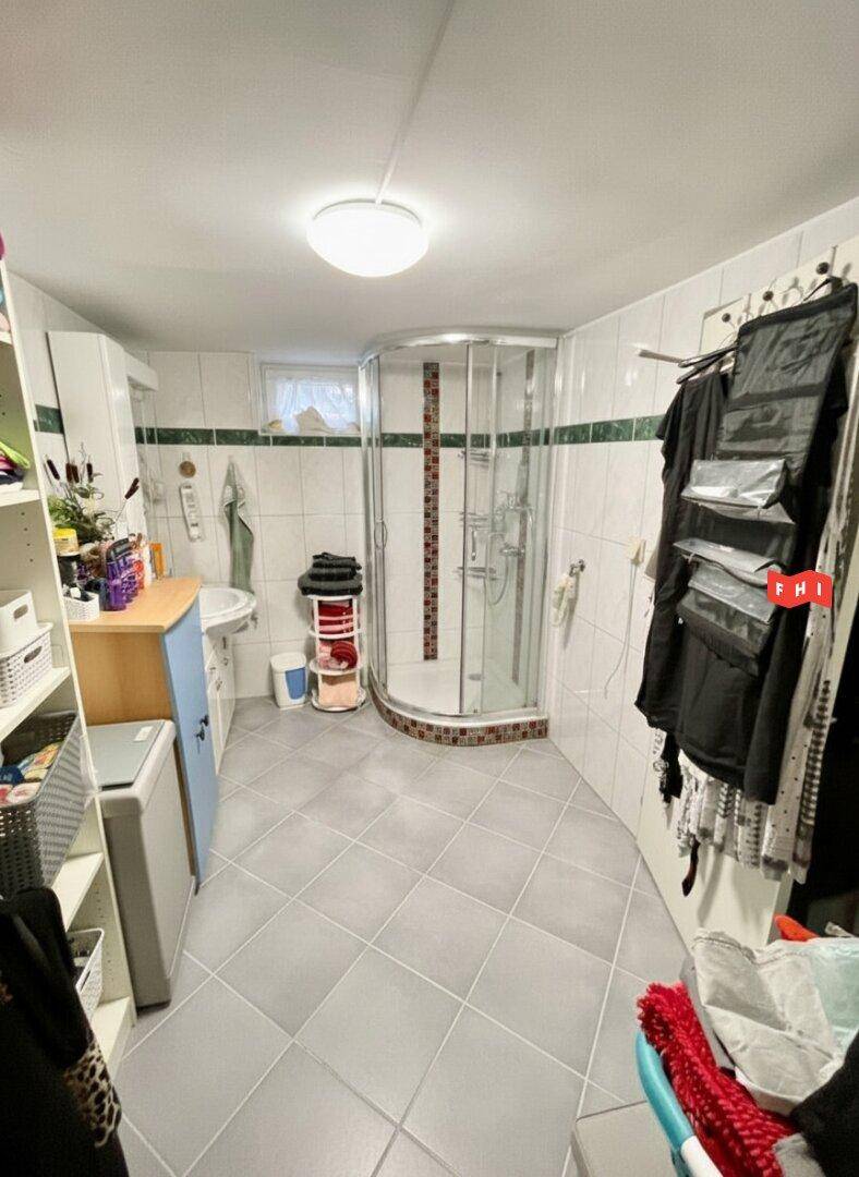 Badezimmer mit Duschkabine, Waschbecken und Stauraum, gefliest in Weiß und Grün.