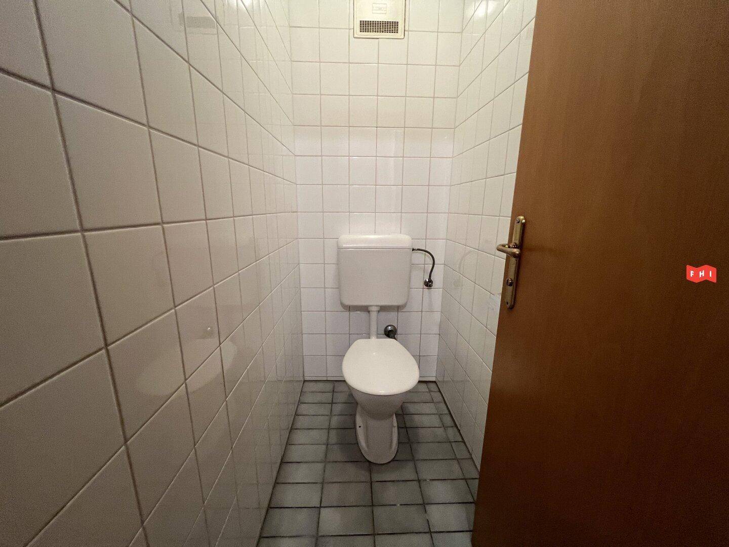 Kleines, gefliestes WC mit Toilette und dunklem Boden, praktisch und sauber gestaltet.