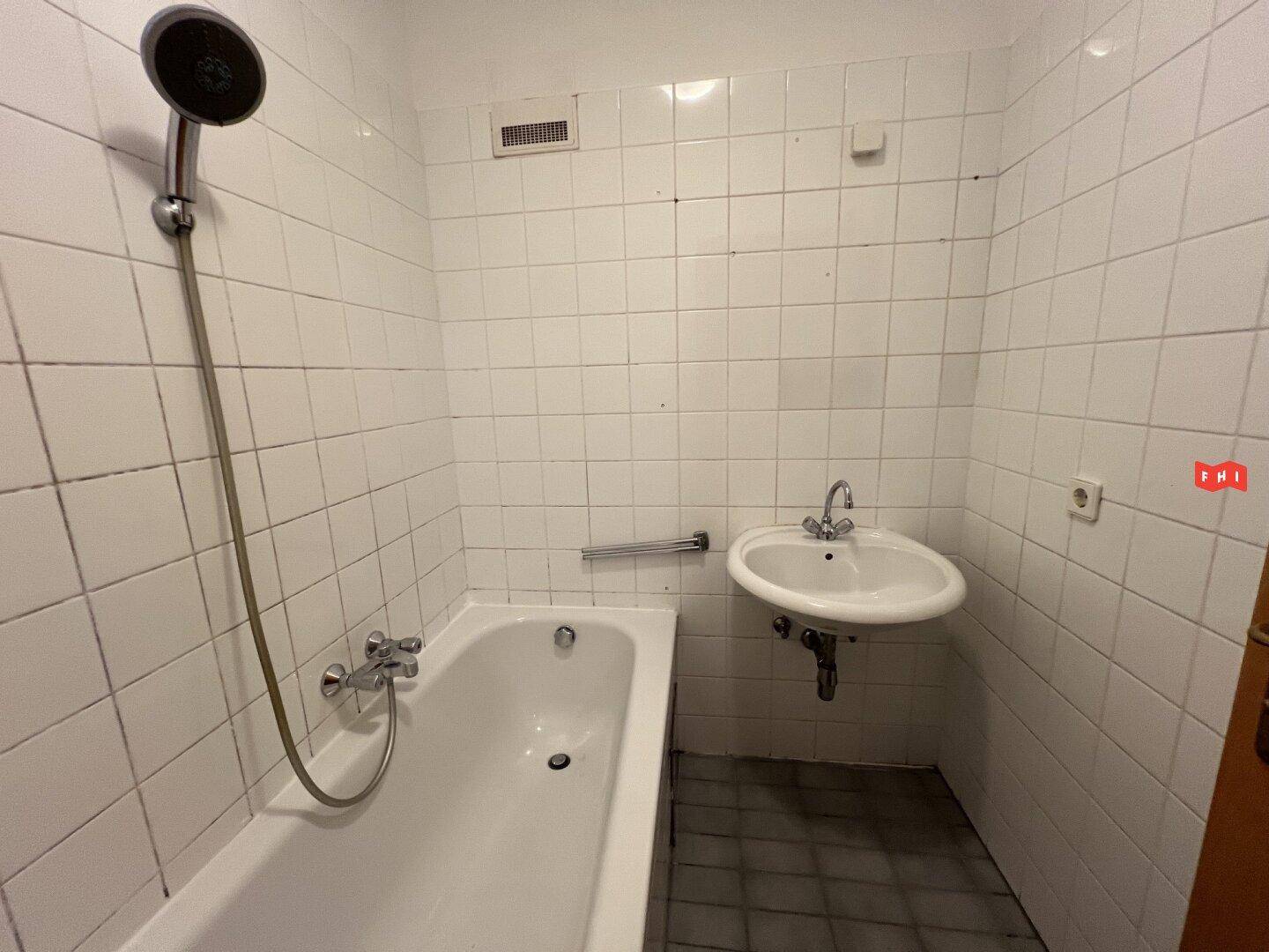 Gefliestes Badezimmer mit Badewanne, Duschkopf und Waschbecken, in einem funktionalen Design gehalten.