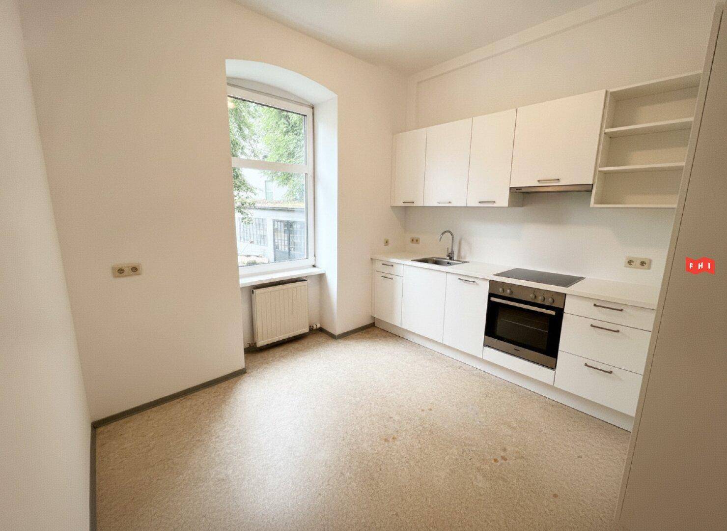 Moderne, helle Küche mit weißen Schränken, Induktionskochfeld und großem Fenster für natürliches Licht.