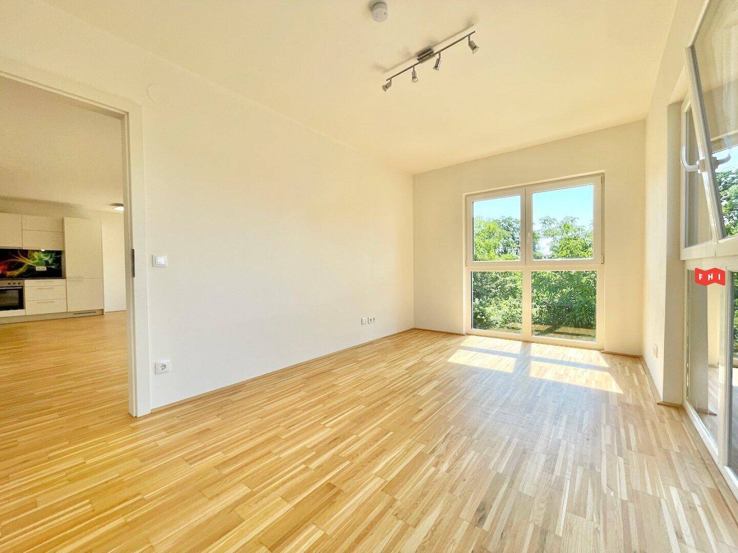 Heller Wohnbereich mit Parkettboden und Blick auf die moderne Küchenzeile im Hintergrund.
