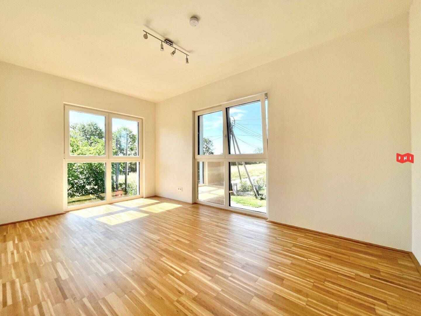 Großzügiges Wohnzimmer mit Parkettboden und großen Fenstern, die viel Tageslicht hereinlassen.