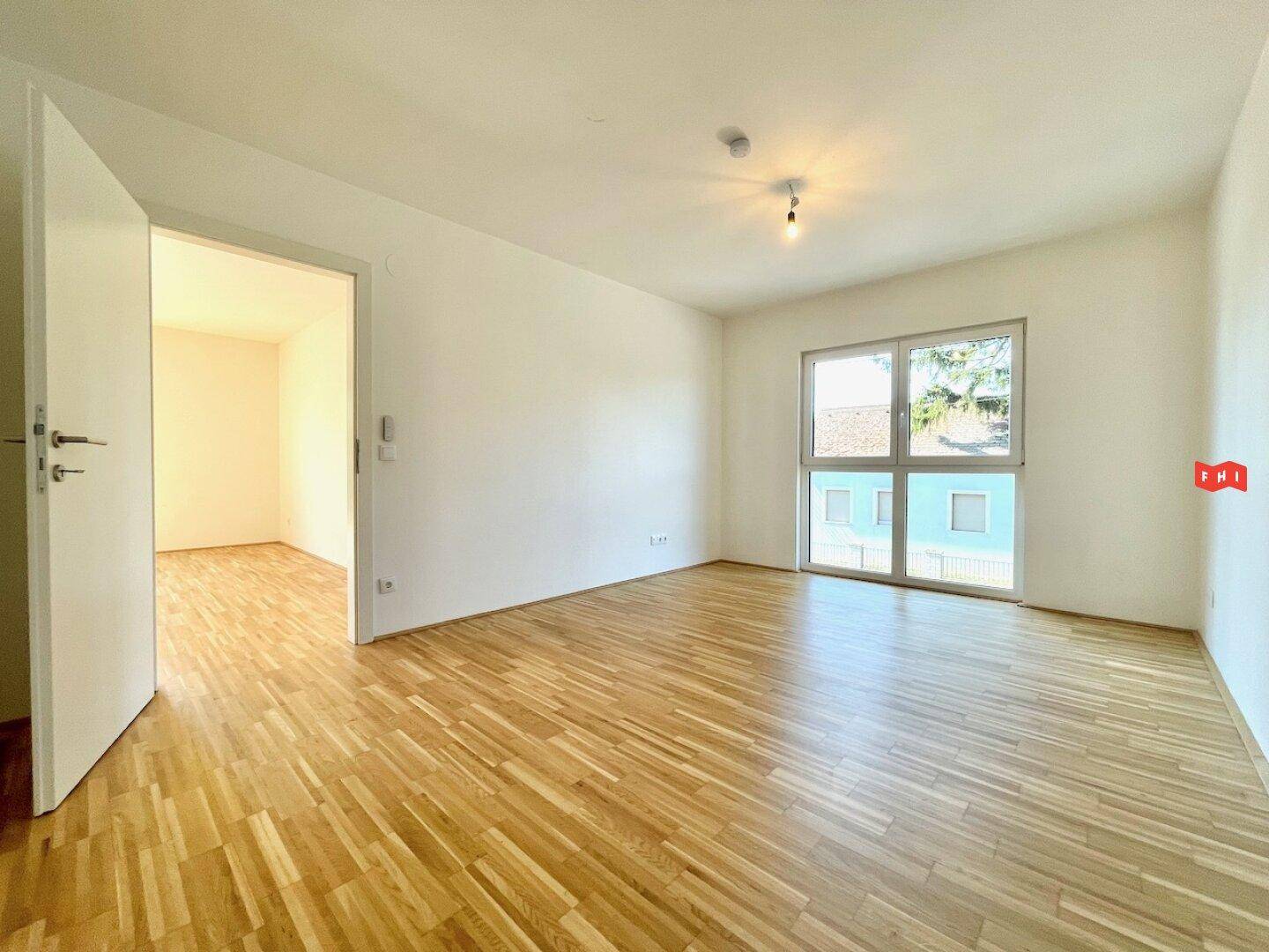 Helles Wohnzimmer mit Parkettboden und Zugang zu einem weiteren Raum, ideal für flexible Nutzung.
