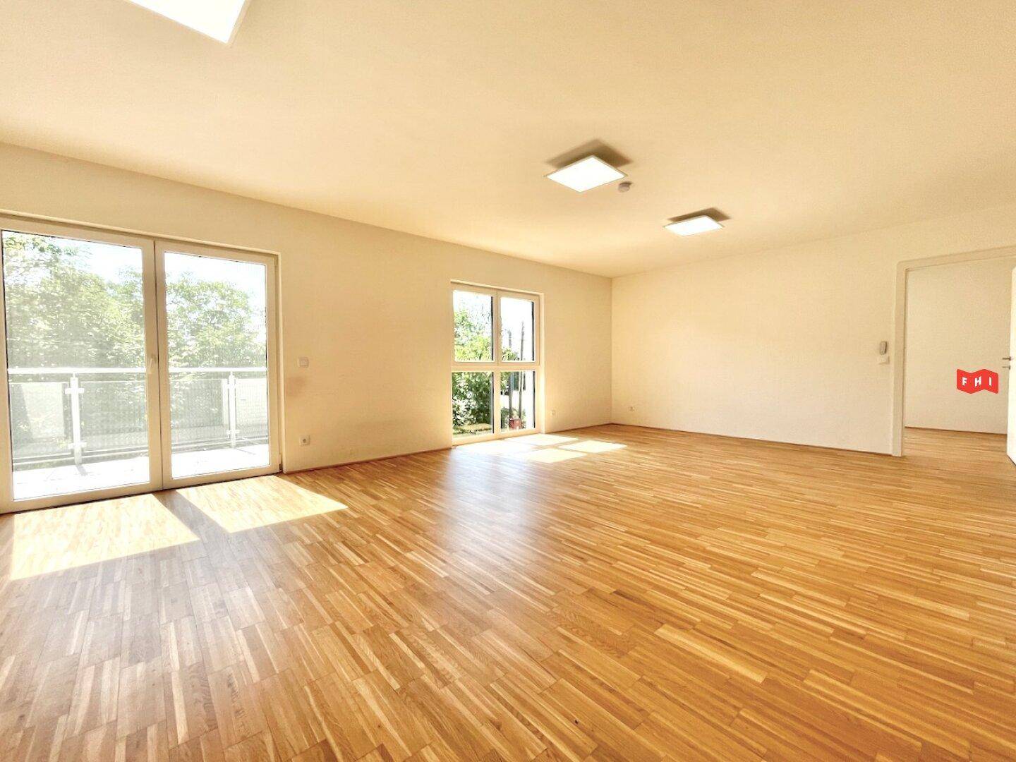 Geräumiges Wohnzimmer mit hellem Parkettboden und Zugang zu einem sonnigen Balkon.