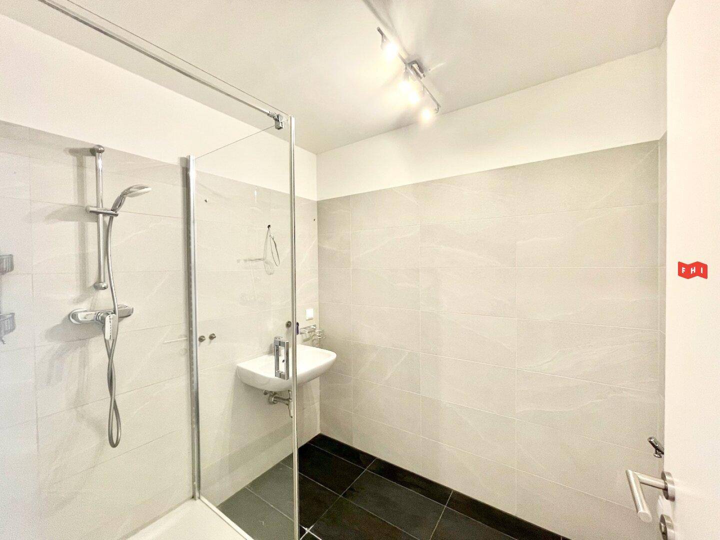 Modernes Badezimmer mit ebenerdiger Dusche, hellen Fliesen und einem einzelnen Waschbecken.