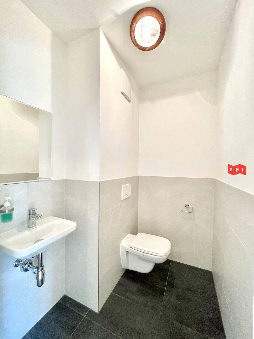 Separates Gäste-WC mit Wand-WC, kleinem Waschbecken und modernen Fliesen.
