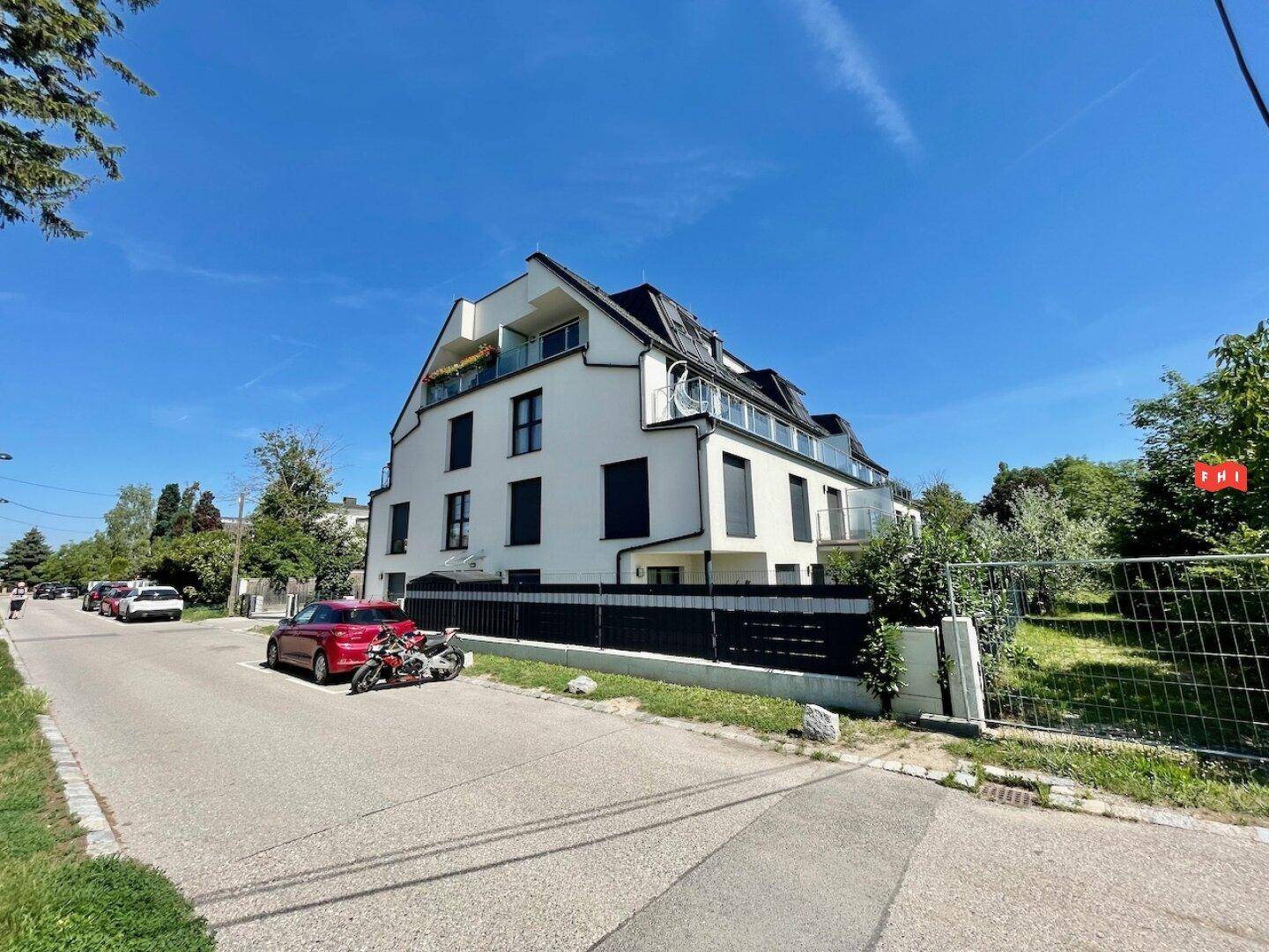 Ansicht des modernen Wohngebäudes von der Straße mit gepflegter Außenanlage und blauer Himmel.