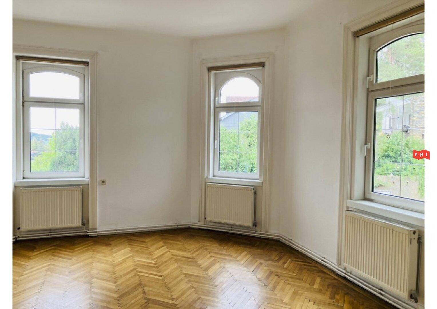 Heller Raum mit Fischgrätparkettboden und hohen Fenstern, die einen Blick ins Grüne bieten.