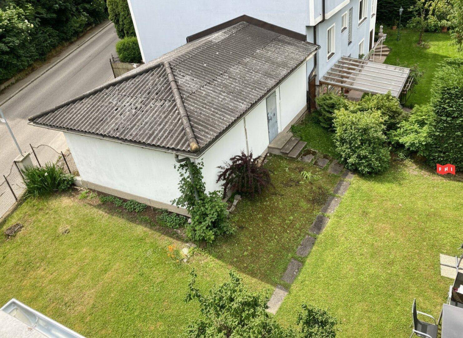 Gartenbereich mit Rasenfläche, einem Nebengebäude und umgebenden Bäumen von oben gesehen.