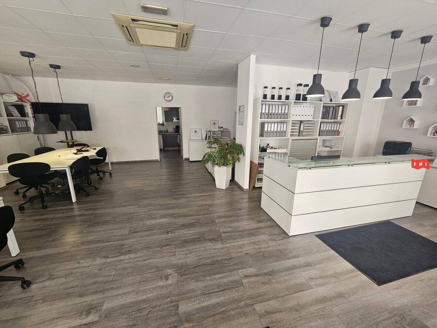 Geräumiges Büro mit Empfangsbereich, Besprechungstisch und Klimaanlage an der Decke.