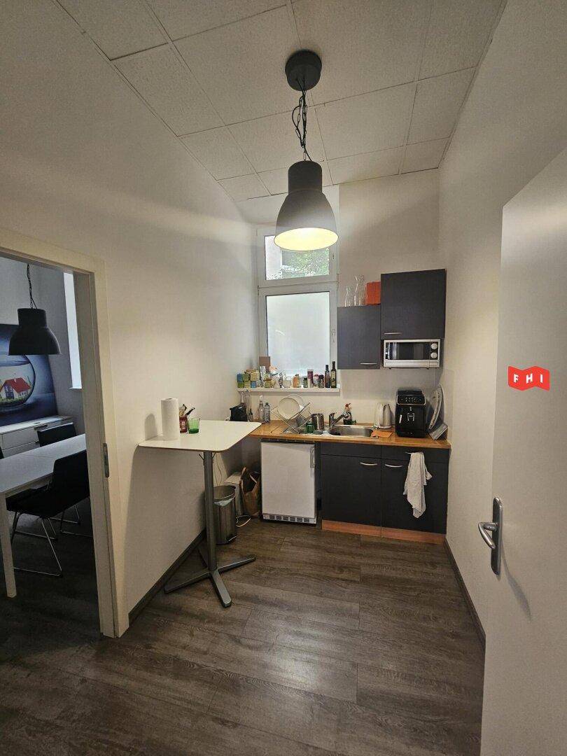 Funktionale Küchenzeile mit dunklen Schränken, Spüle, Mikrowelle und kleinem Kühlschrank.