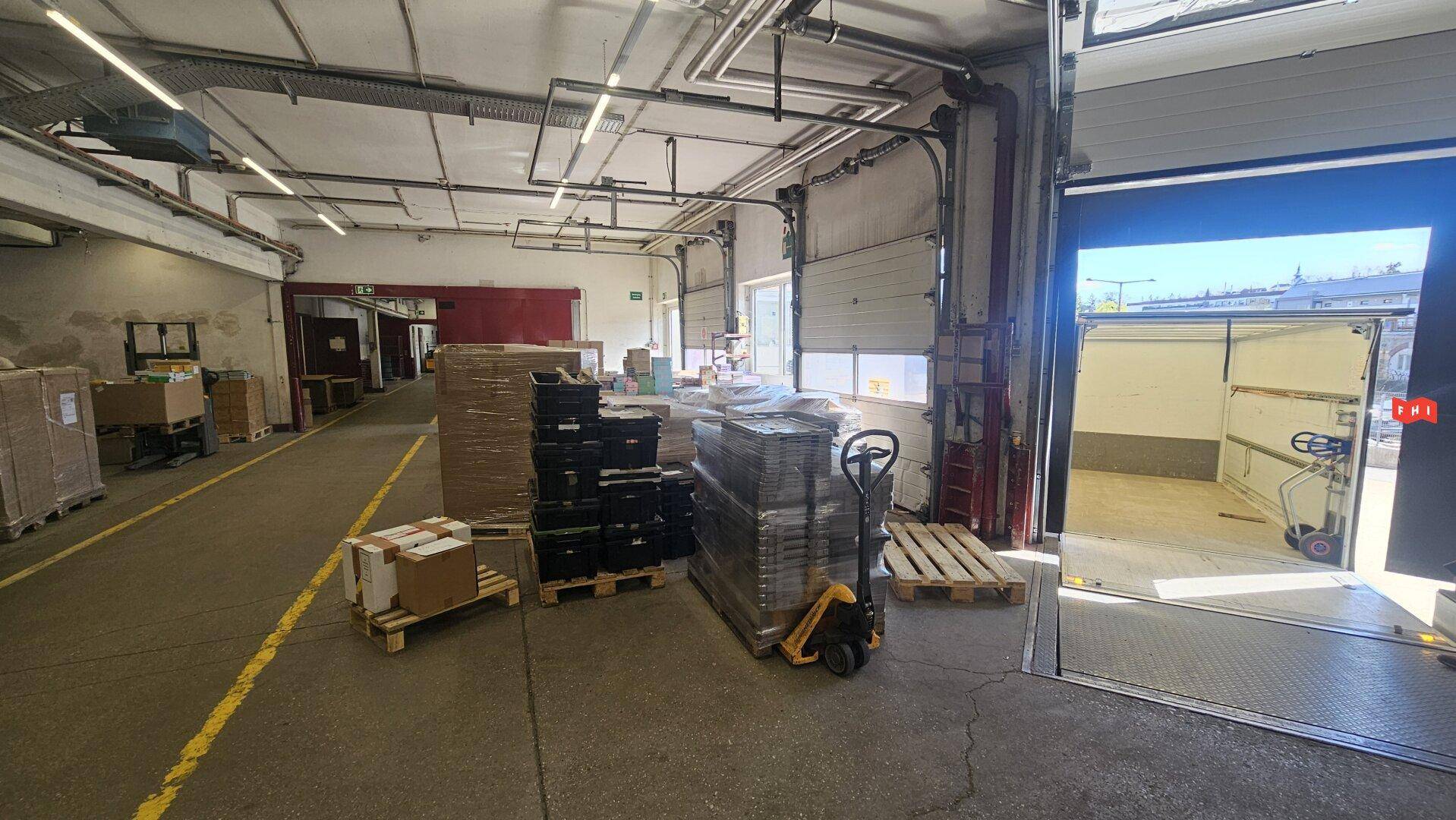 Ladebereich einer Lagerhalle mit geöffnetem Rolltor, Paletten und Waren für den Transport.