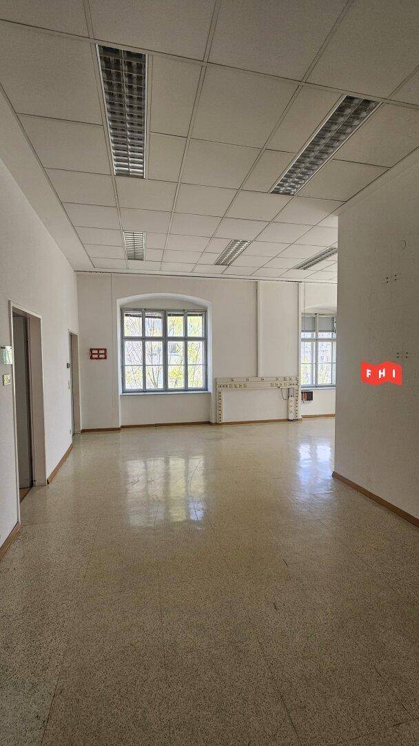 Heller Büroraum mit Terrazzoboden, abgehängter Decke und großen Fenstern, die Tageslicht hereinlassen.