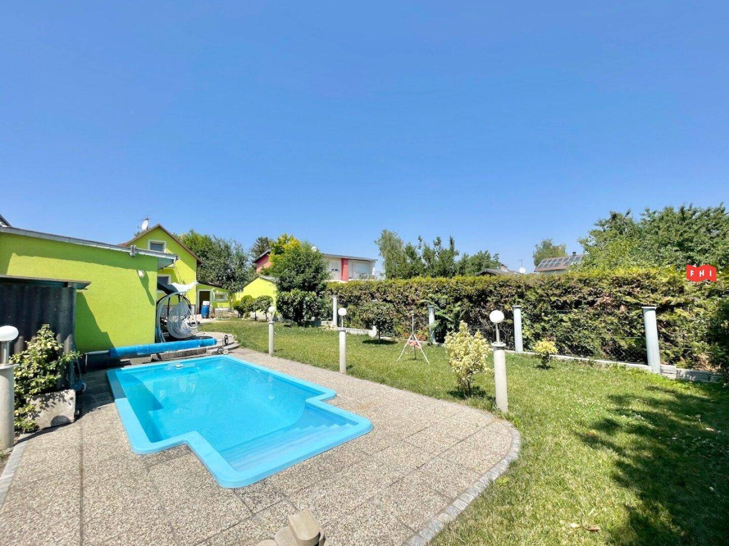 Gartenbereich mit rechteckigem Pool, gepflastertem Rand und einer Hecke im Hintergrund.