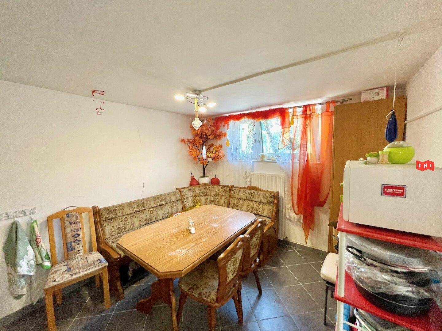Essbereich in der Küche mit traditioneller Eckbank, Holztisch und Fenster mit Vorhängen.